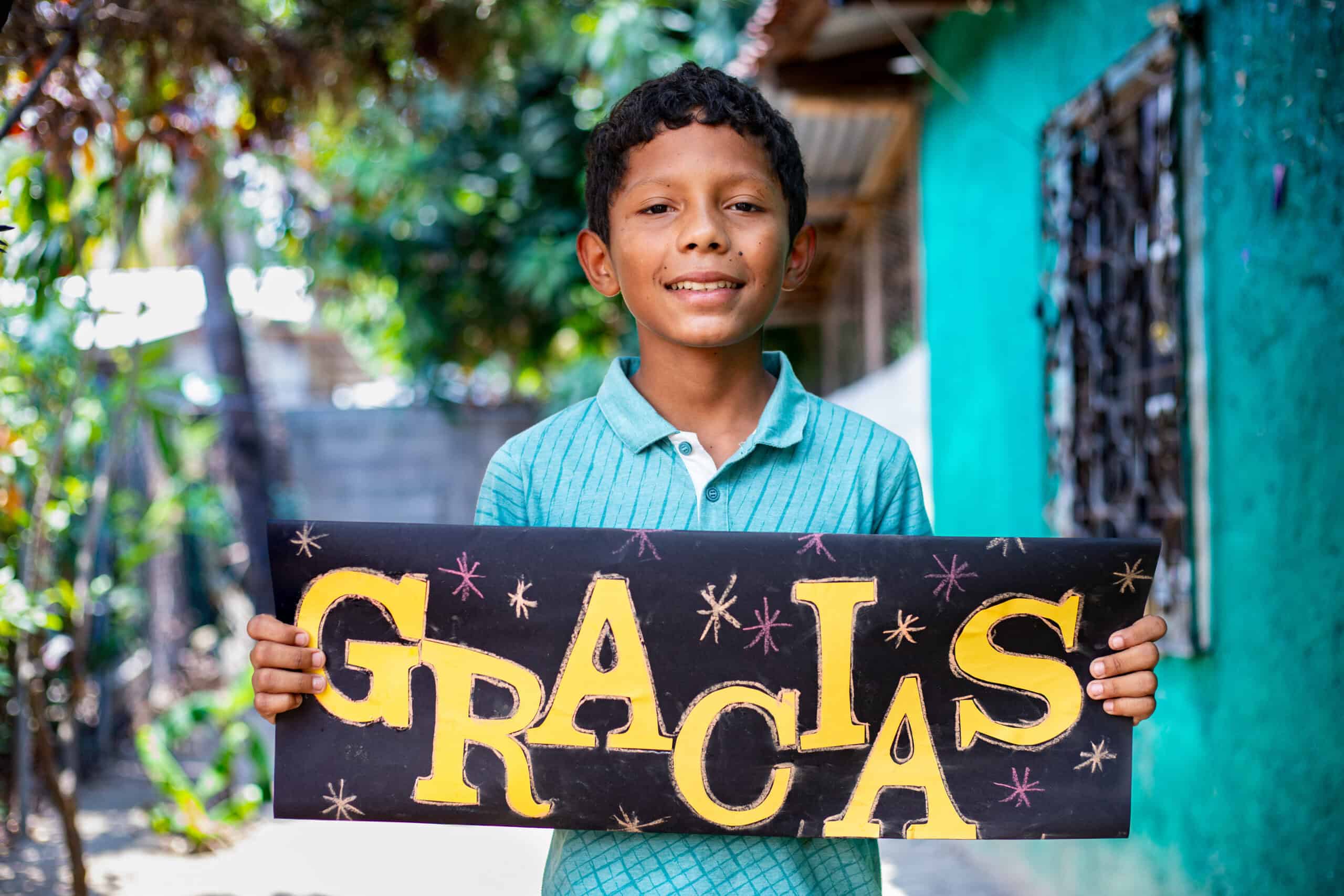 A young boy holds a sign that says "Gracias" in bright yellow. 4 stories of gratitude from Compassion kids. 