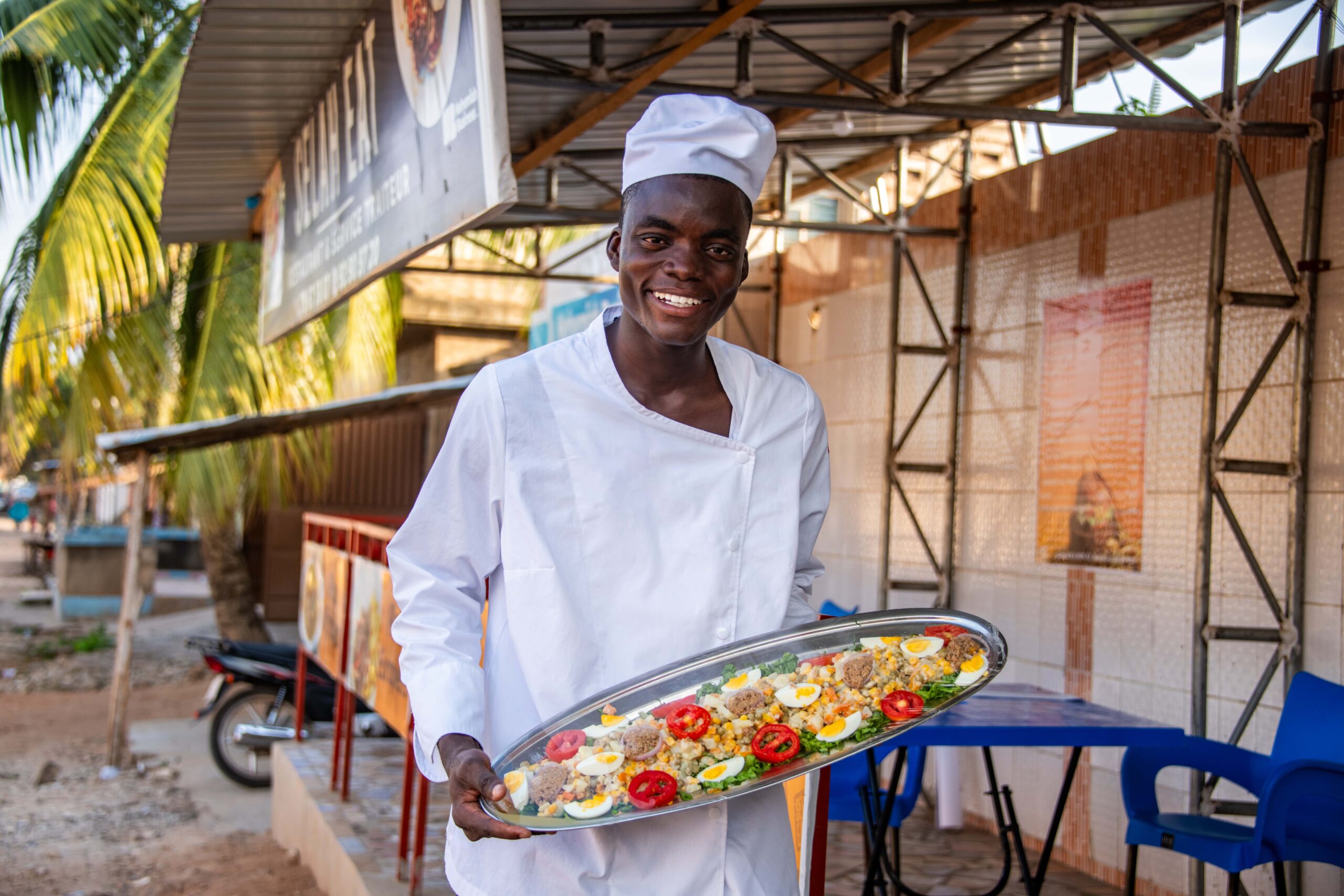 Felicien, a Compassion alumna, stands wearing his chef hat and a white coat holding a silver platter of food. 7 Delicious & Unique Recipes From Around the World