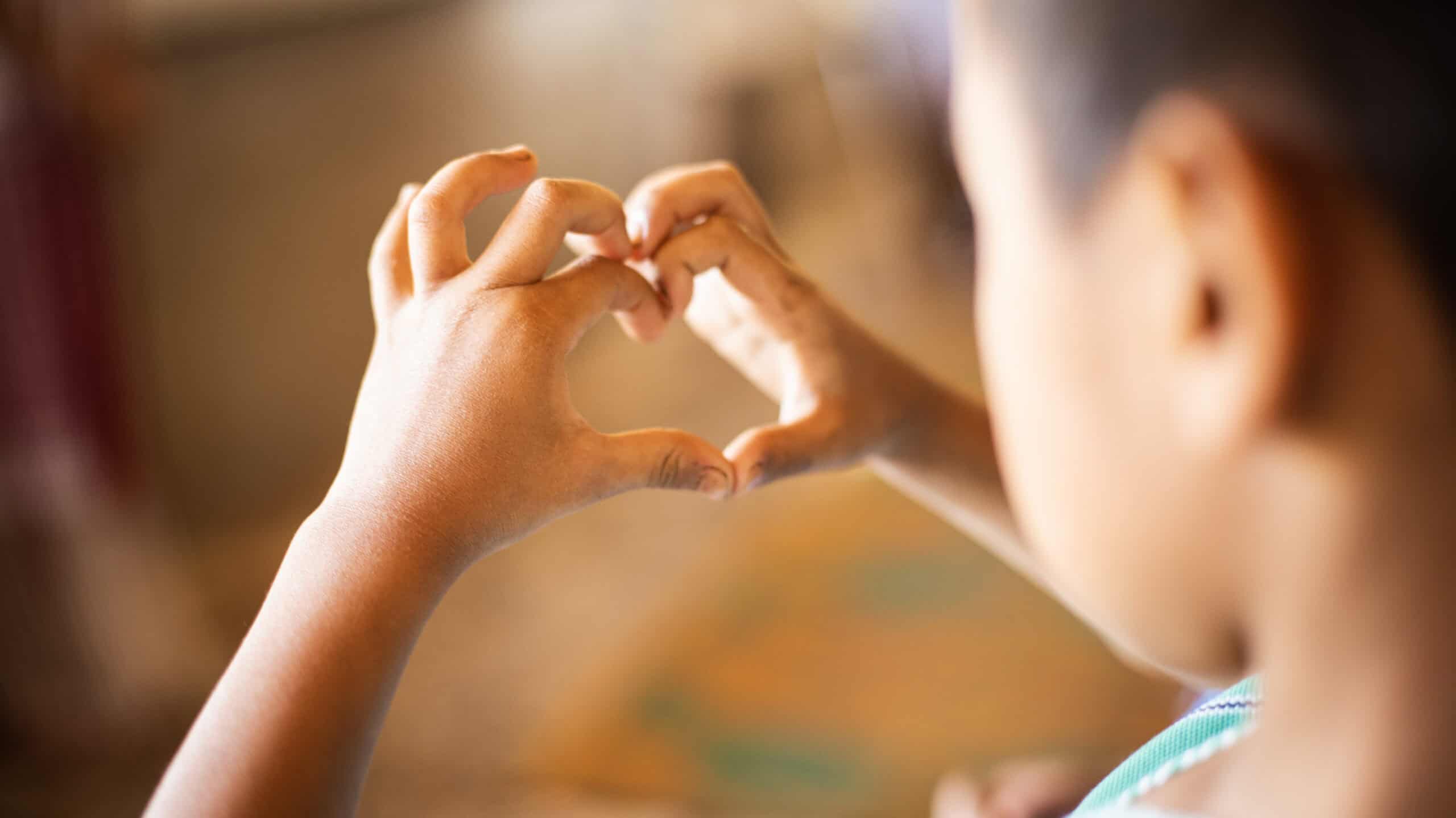 Child holds hands in the shape of a heart. 