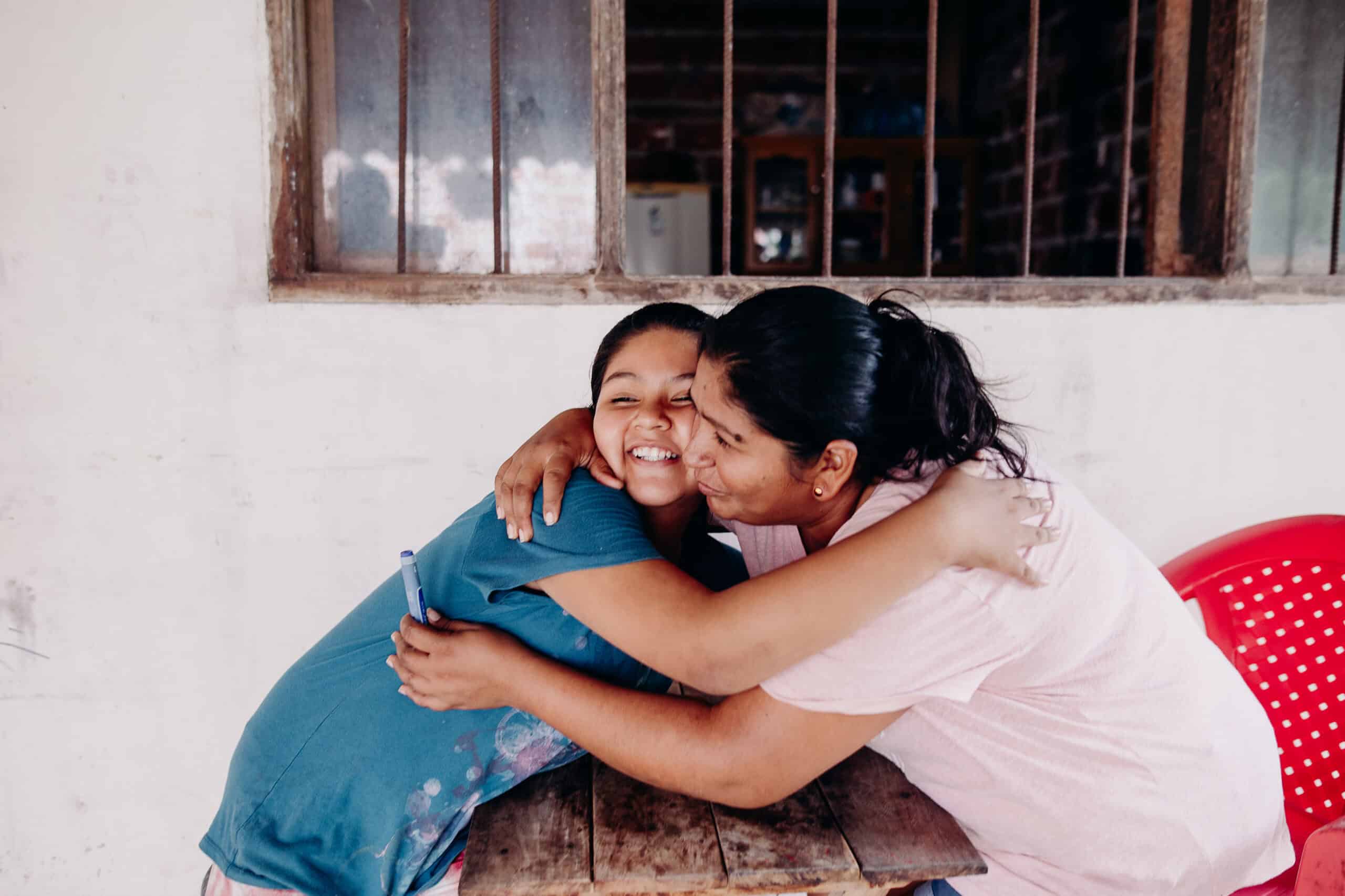 A young girl and an older woman hug and smile. The older woman holds a blood sugar tester.