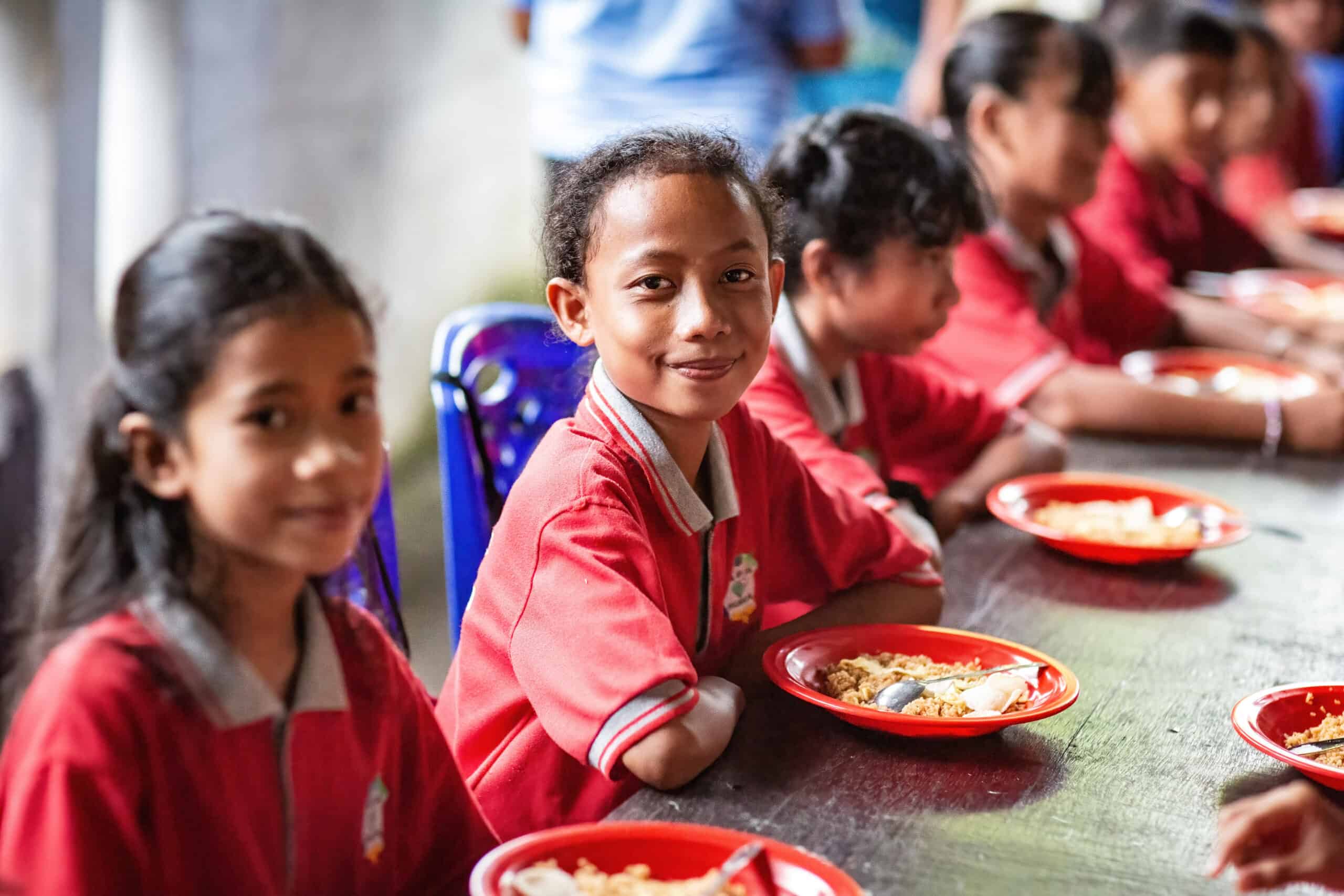 A group of children sitting at a table, representing the community impact of Frizky’s initiative to create a nutritious food course and a training program for Compassion youths.