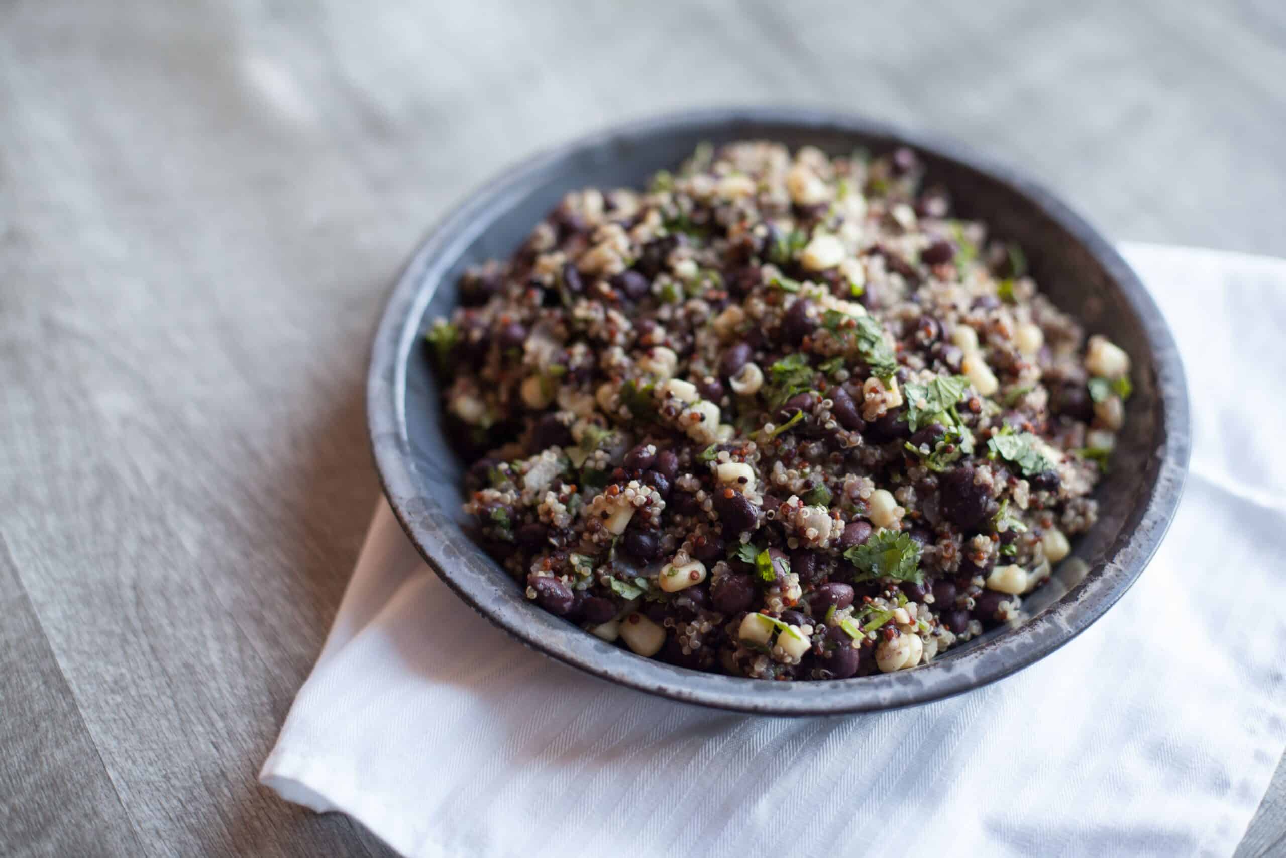 Quinoa and black bean salad sits in a gray bowl on top of a white handkerchief.