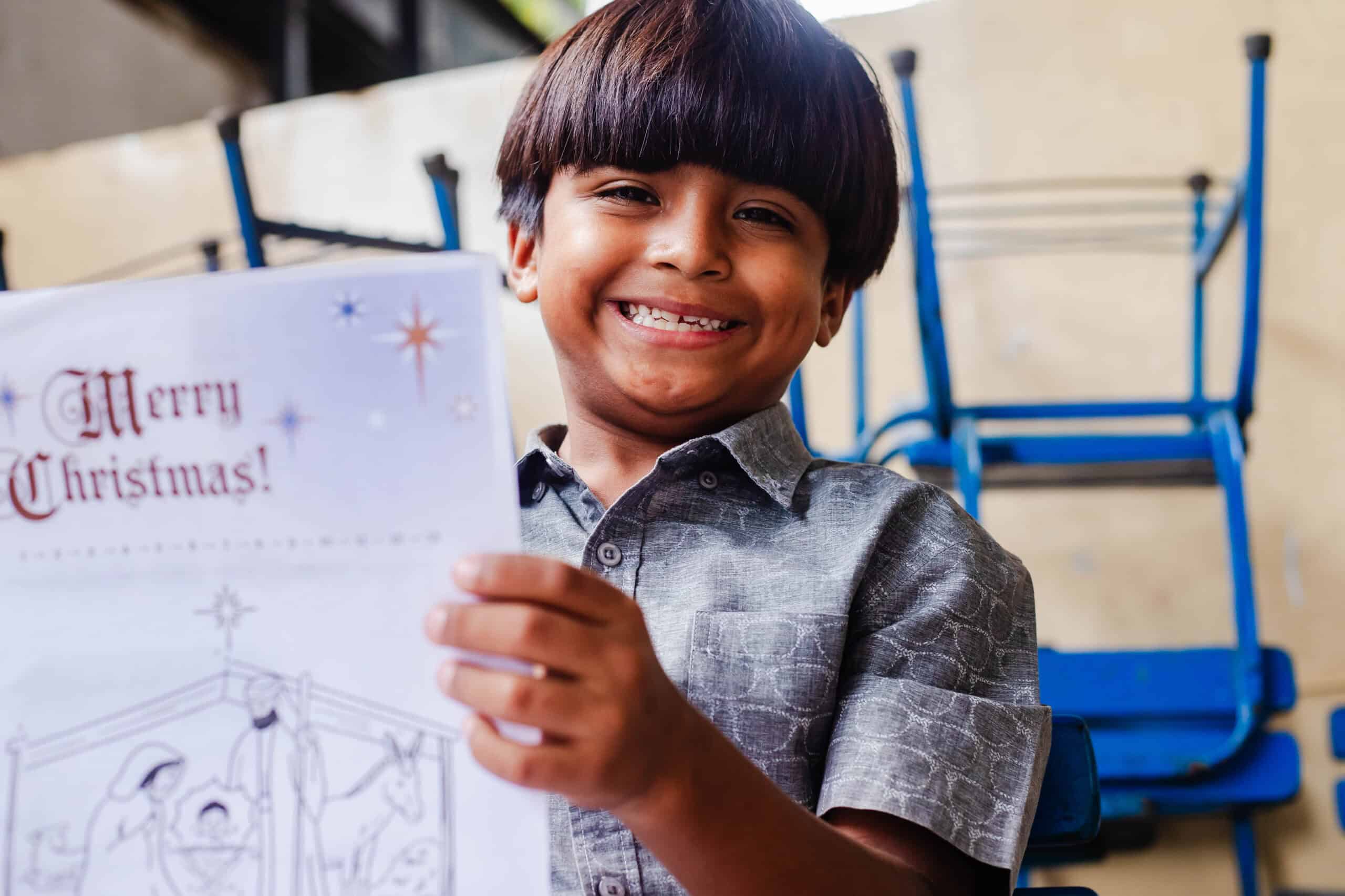 A little boy holds a piece of paper and smiles at the camera