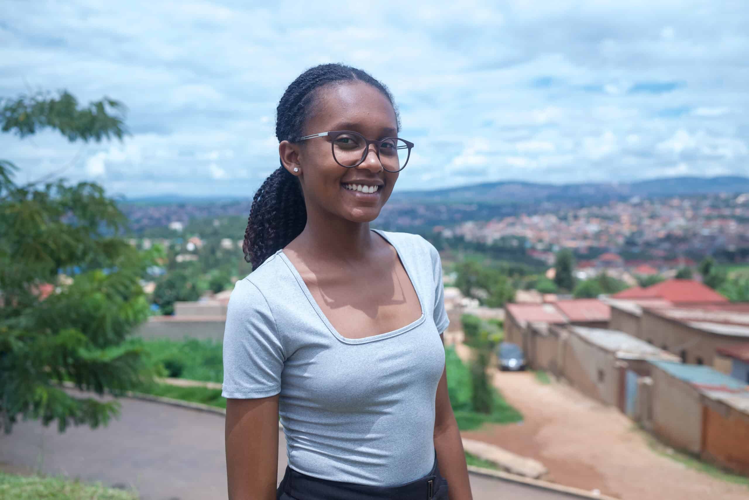 A young girl wearing a blue shirt smiles for the camera in front of a beautiful landscape.