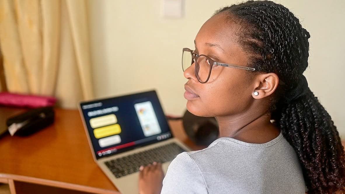 A young woman sits in front of a computer and looks off to the left.