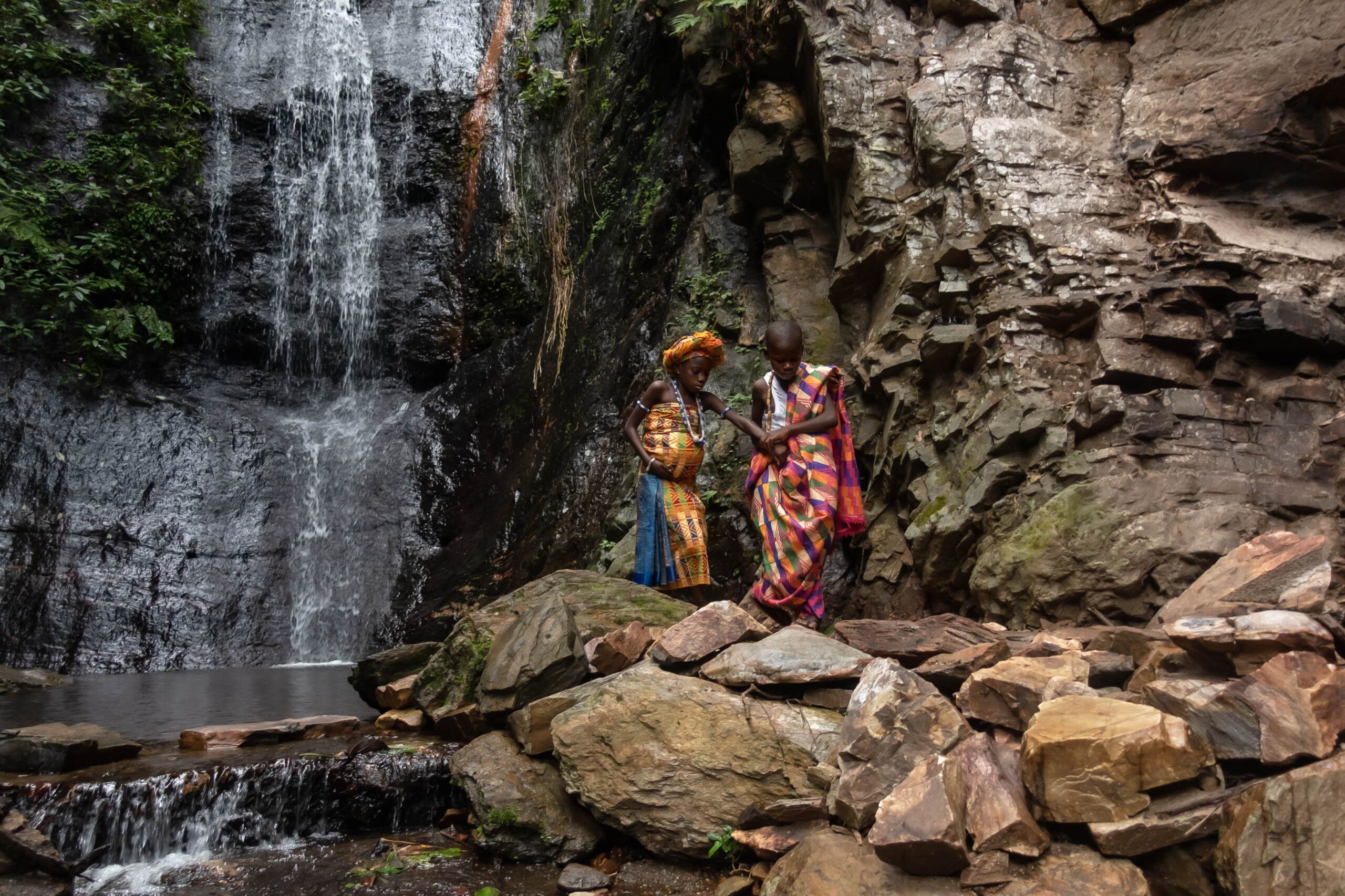 CC-TG0946-Nativity-036-2506-min A boy and girl in traditional dress hold hands as they cross the rocky terrain of a waterfall.
