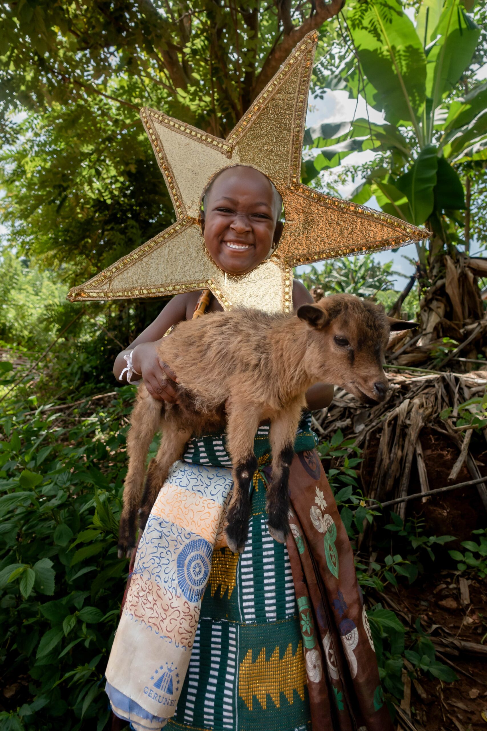 A girl dressed as the star from the Nativity Story stands outside, smiling with a baby goat in her arms.