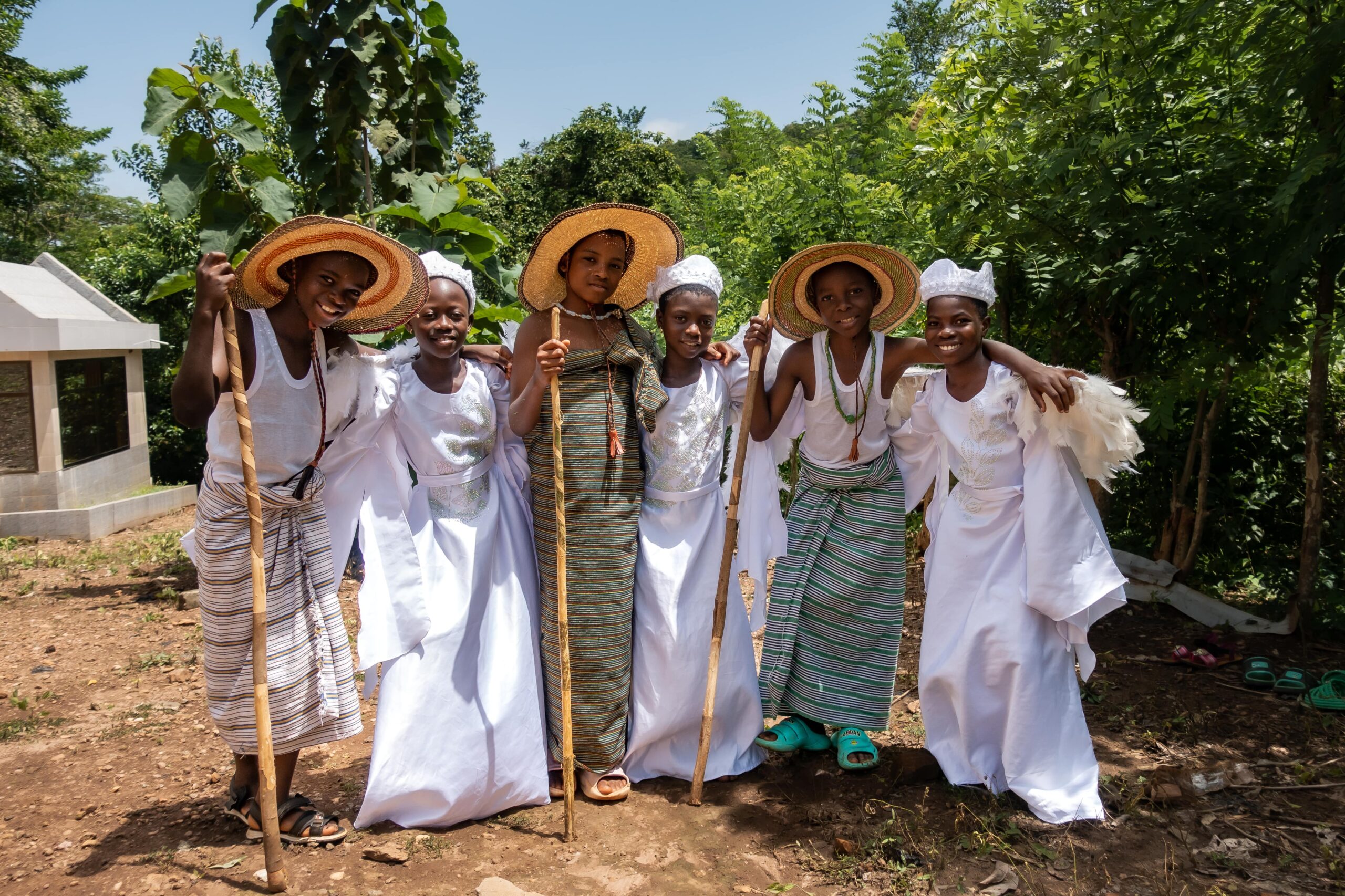 CC-TG0946-Nativity-119-2506-min A group of children dressed as the angels and shepherds from the Nativity Story smile together, standing outside in front of trees.
