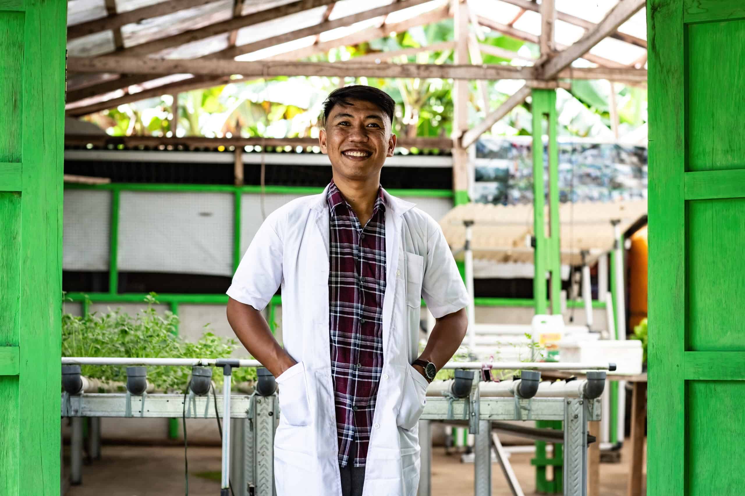 A young man wearing a lab coat stands between two bright green doors and smiles for the camera.