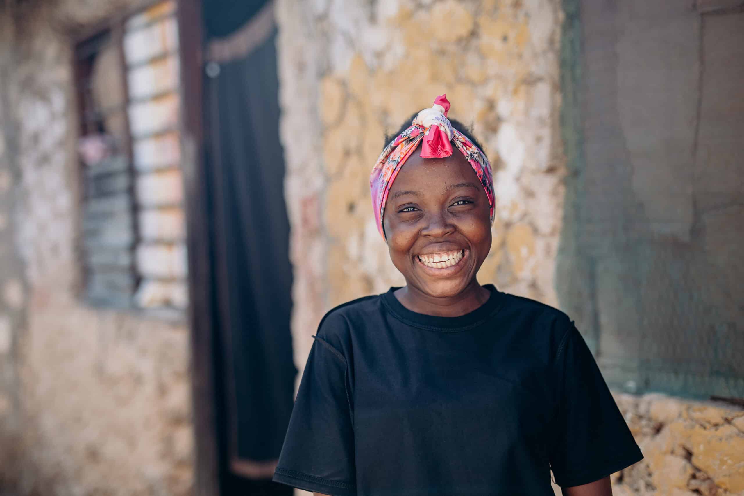 A young girl wearing a black shirt and brightly patterned headband smiles for the camera.