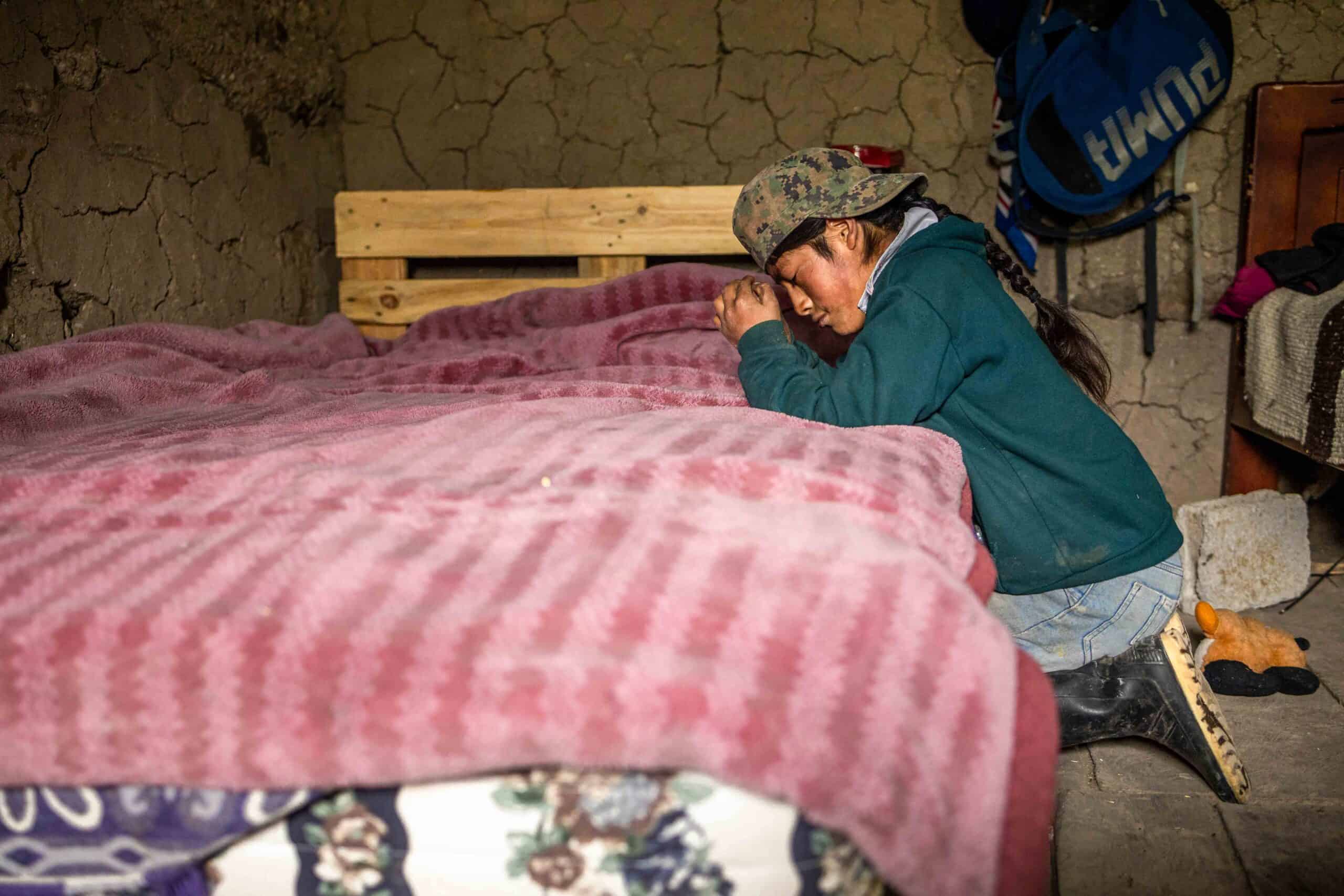 A young boy kneels at the size of his bed as he prays.