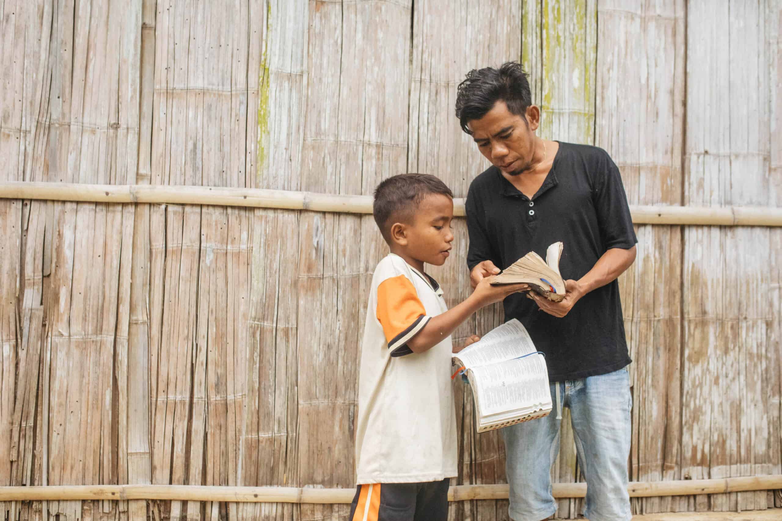 A young boy holding a Bible points out a page in a Bible another taller man is holding.