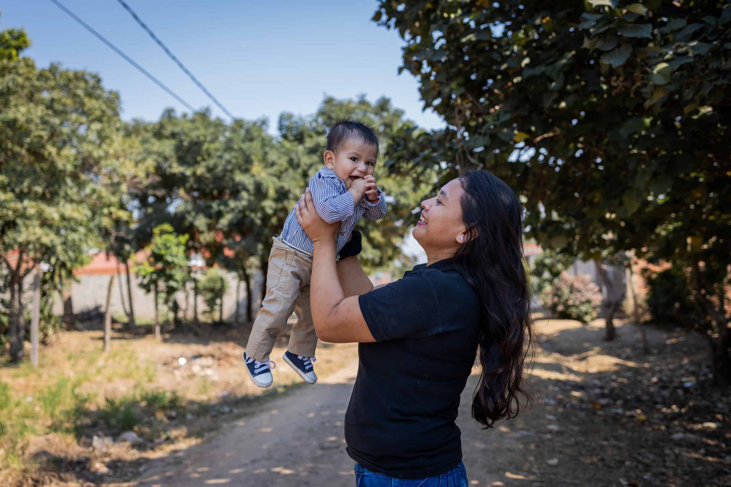 A mother holds her baby in front of her and smiles at him.