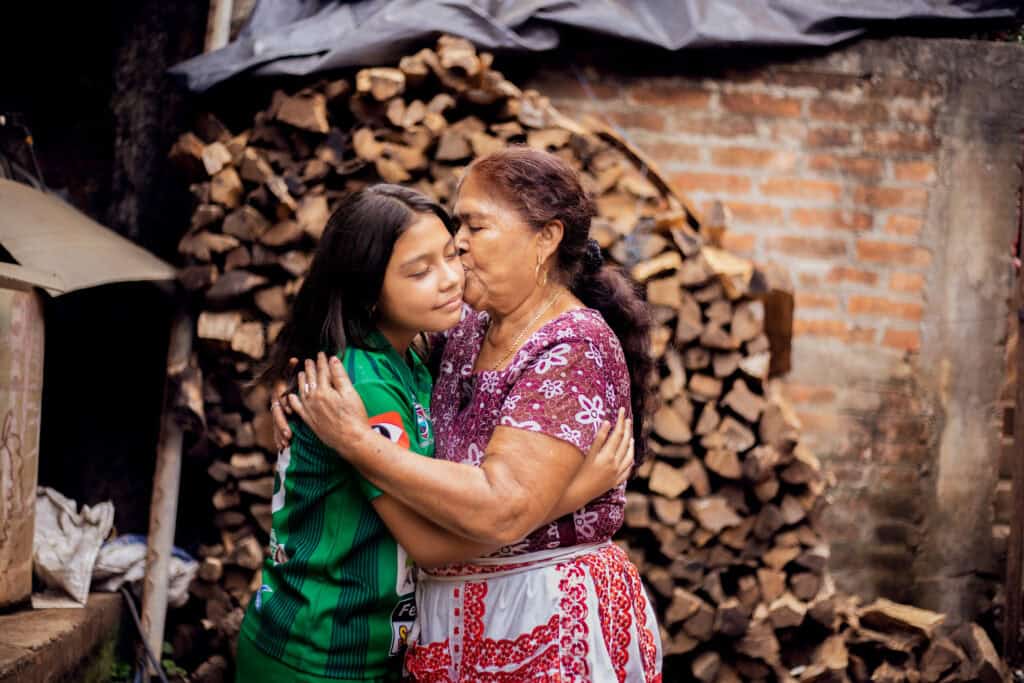 An older woman hugs a younger girl wearing a soccer uniform.