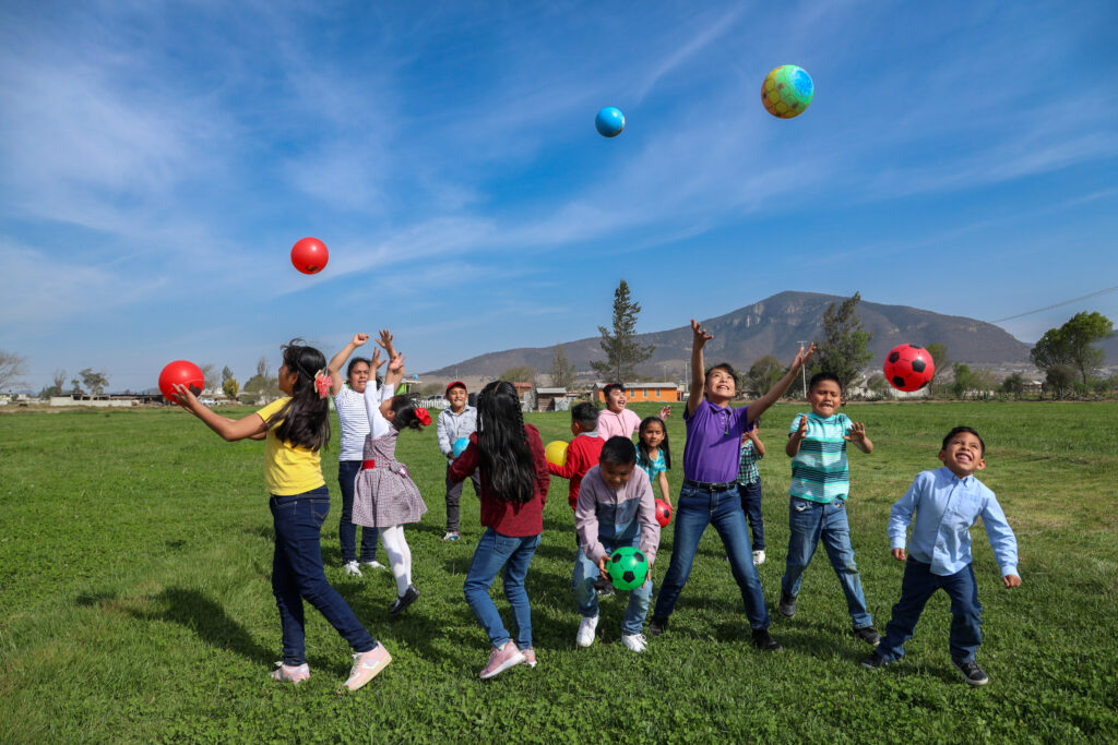 A group of children jump and throw balls into the air while smiling and laughing.