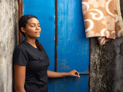 A young girl leans against a wall with her eyes closed.