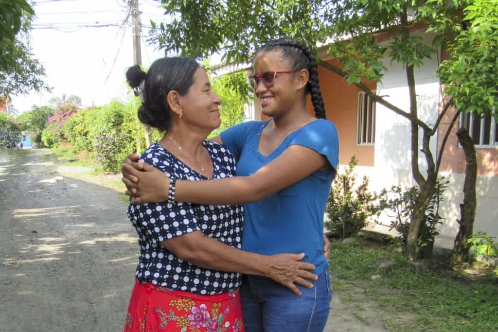 An older woman and a teenage girl smile at one another while hugging.