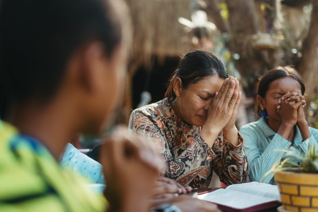 Three women fold their hands in front of their faces with their eyes closed as they pray.