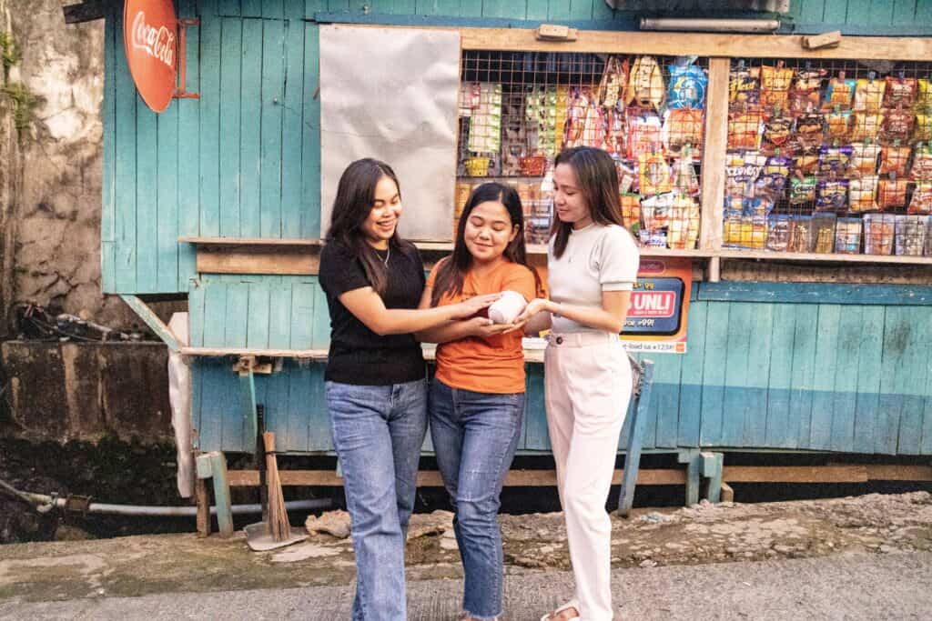 Image shows three girls standing together and smiling. The girl in the middle has a bandage wrapped around her arm.