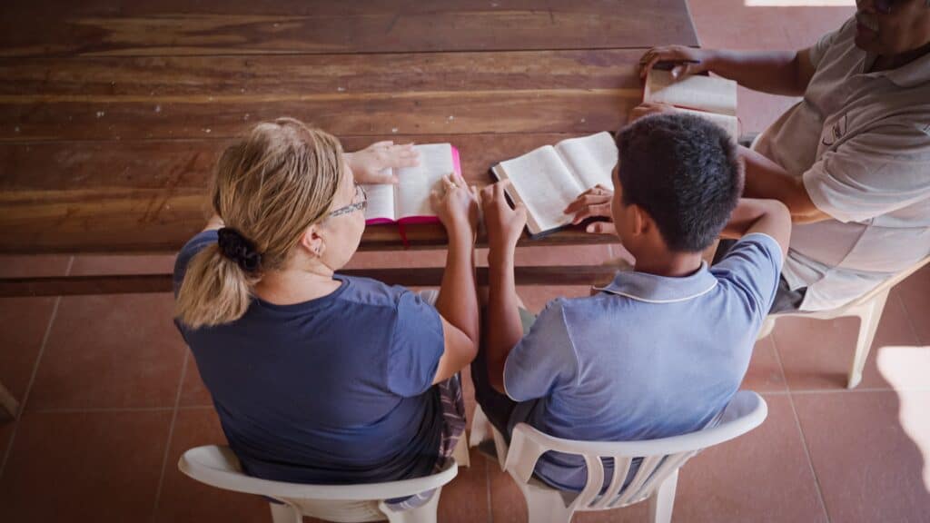  An older woman and a teen sit at a wooden table with their Bibles out in front of them.