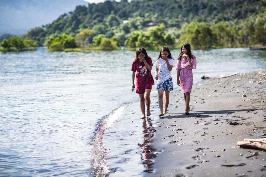 Three young girls walk alongside the shore while laughing.