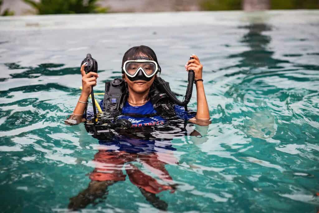 A young girl wearing goggles and dive gear floats in a pool.