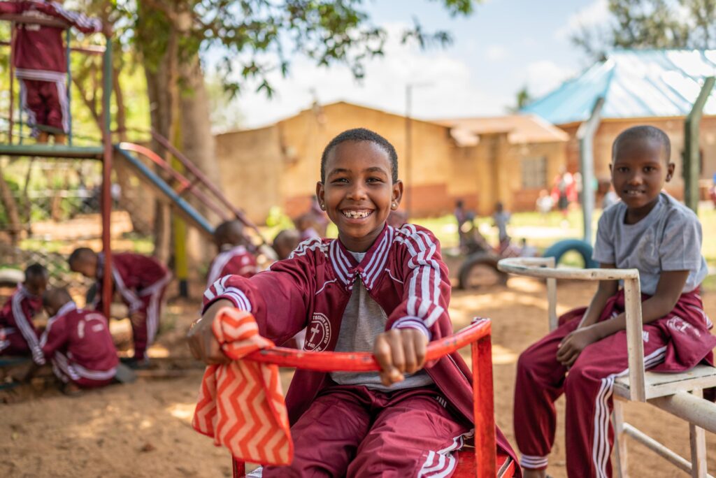 Two young boys play on playground equipment while smiling for the camera.