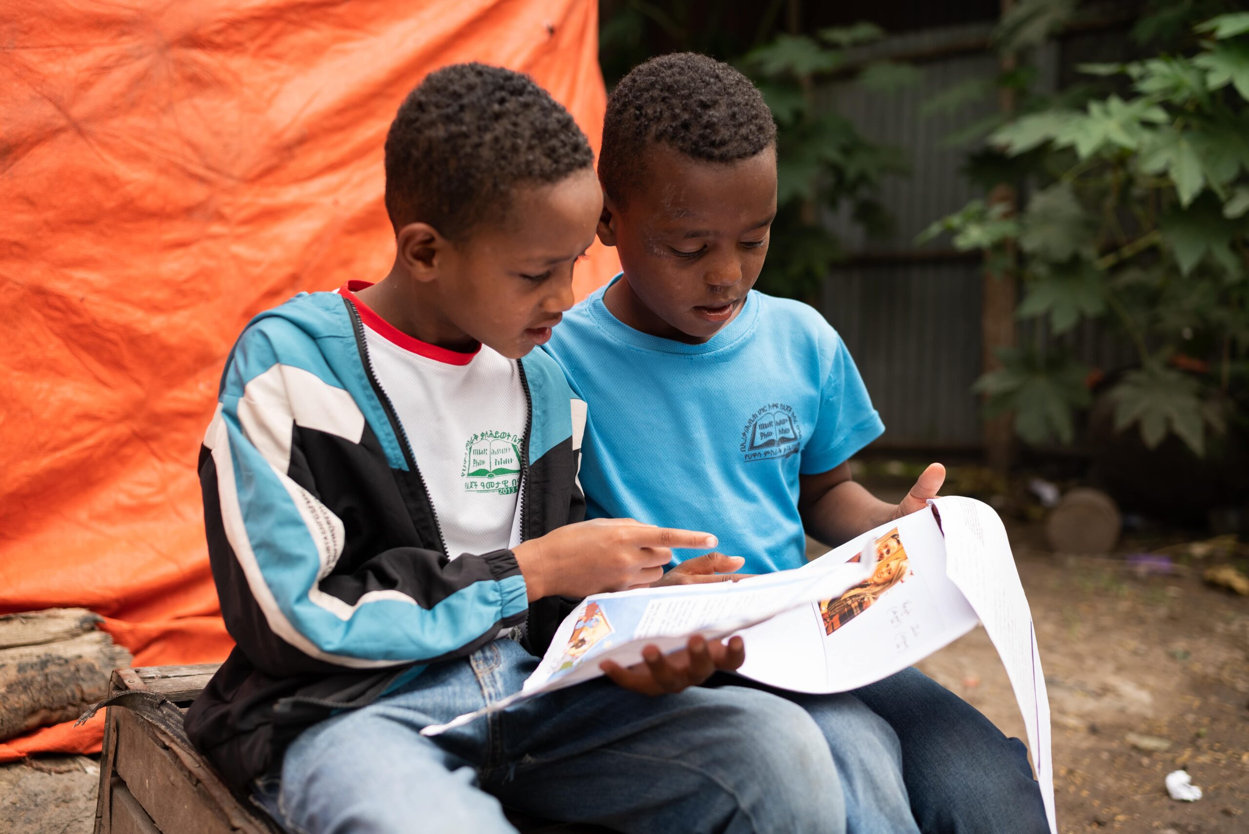 CC-ET0318-FamilyGift-011-2305-min Two young boys sit next to each while reading letters and smiling.