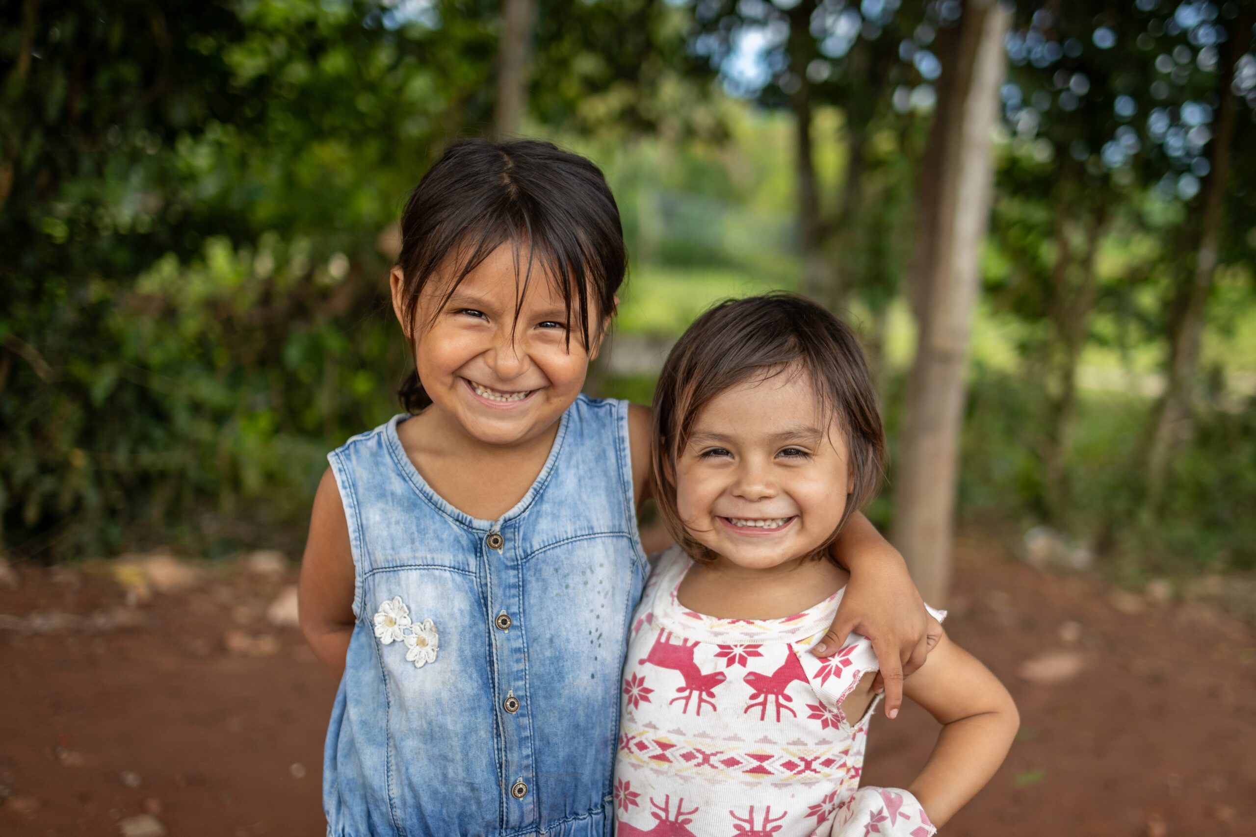 Two little girls stand with an arm around each other smiling at the camera.