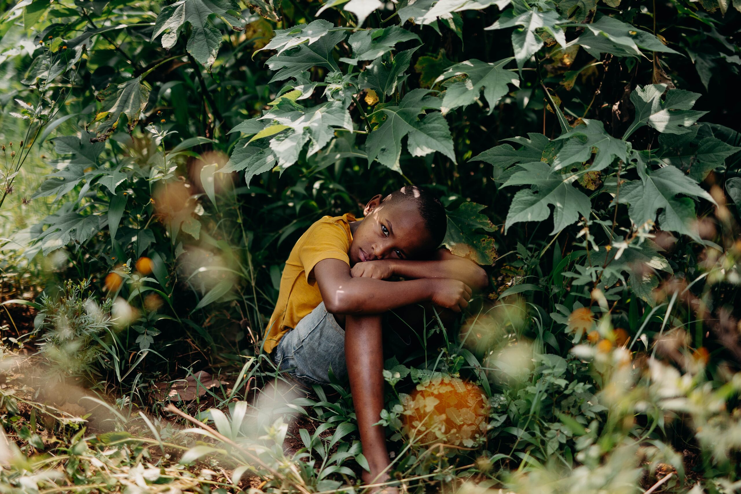 CC-RW0626-44-Alumni-2403-min A young boy sits beneath a tree with his knees up under his chin.