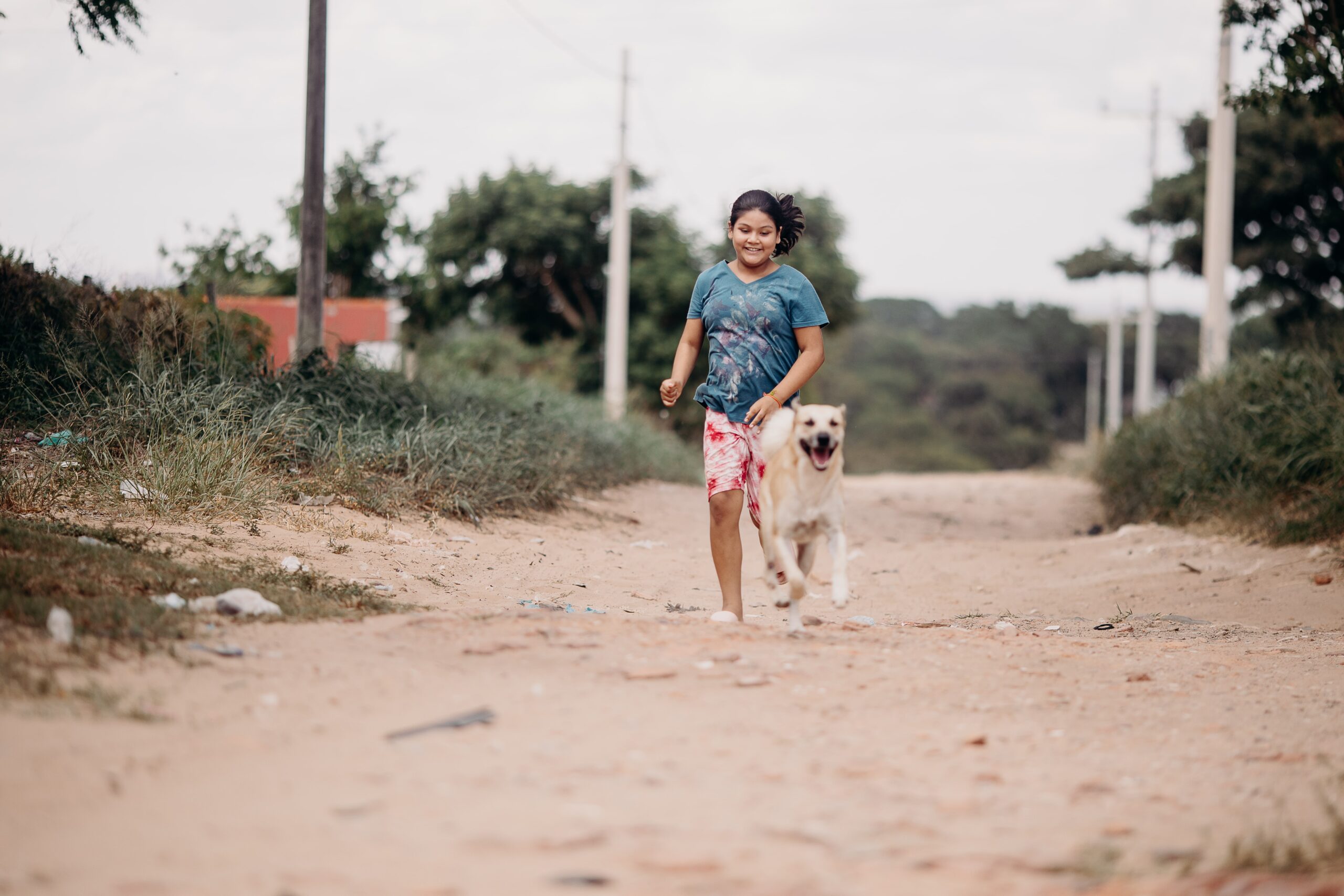 Q2_HB_Feature_Wendy_53-min A young girl skips alongside a dog down a dirt road while smiling.