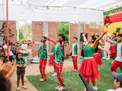 Young adults in red and green costumes dance at a Christmas celebration event. Confetti is in the air.