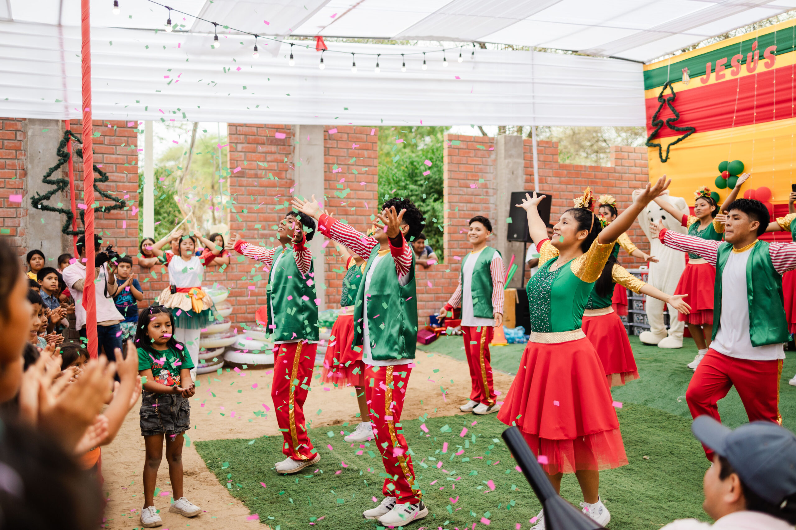 Young adults in red and green costumes dance at a Christmas celebration event. Confetti is in the air.