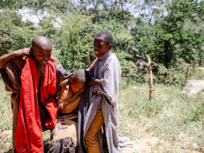 Two African boys help another African boy up off the ground.